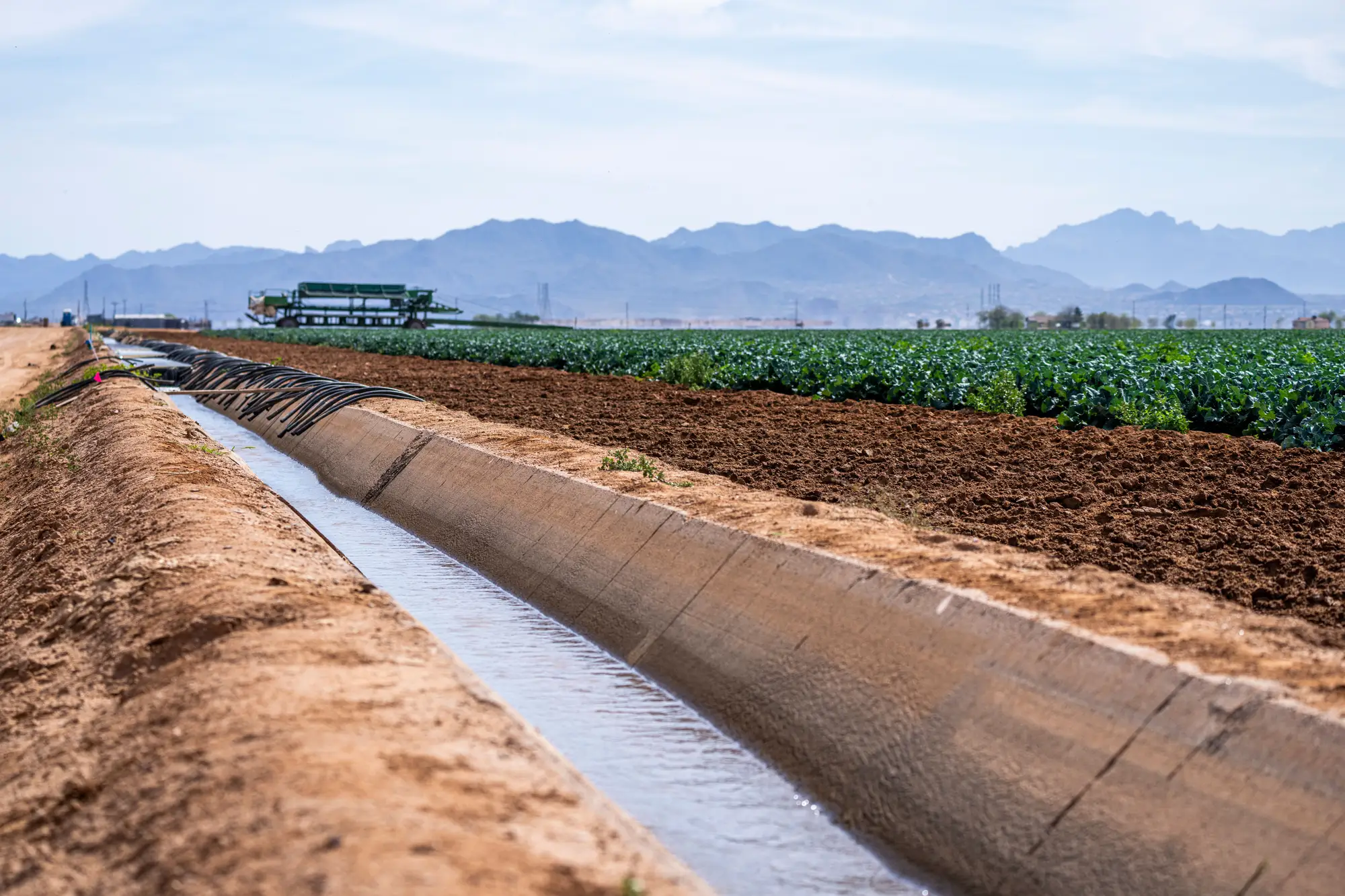 A concrete-lined irrigation channel running beside a cropped field, mountains in the distance